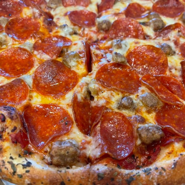 Close-up of a pepperoni and sausage pizza from The Mad Sicilian, with melted cheese and a crispy crust.