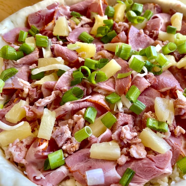Close-up of a pizza with ham, pineapple, and green onions before baking.