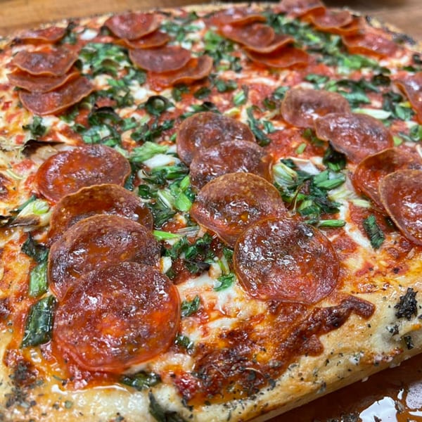 Close-up of a pepperoni pizza from The Mad Sicilian, topped with melted cheese and green herbs.