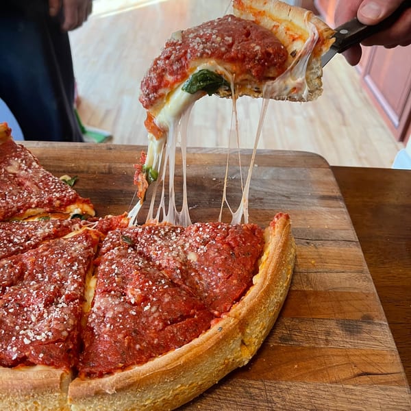 A slice of The Mad Sicilian's deep-dish pizza, with melted cheese stretching, being lifted from the pan.