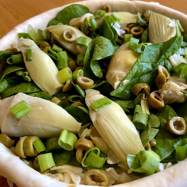 Close-up of a Sicilian dish with artichoke hearts, spinach, green onions, and sliced olives.