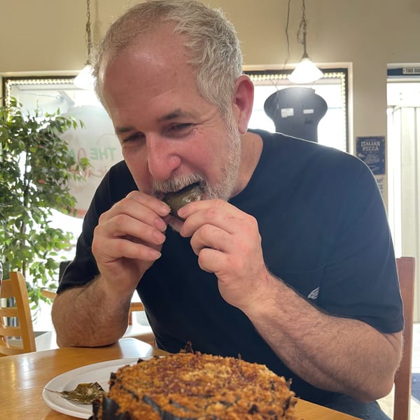 A man in a black shirt happily bites into a cannoli at The Mad Sicilian restaurant.