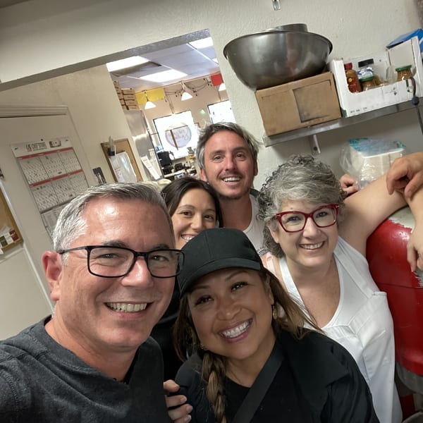Five smiling people, likely staff, pose for a selfie in a restaurant kitchen at The Mad Sicilian.