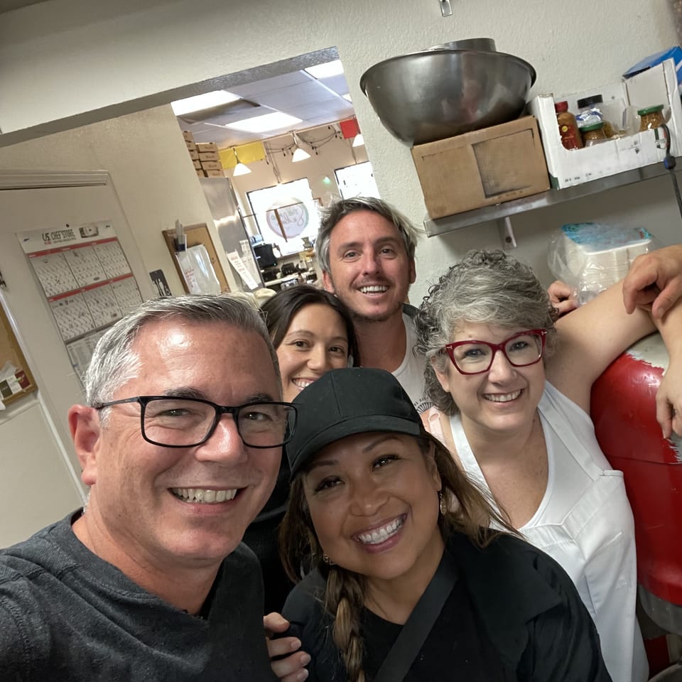 Five smiling people, likely staff, pose for a selfie in a restaurant kitchen at The Mad Sicilian.